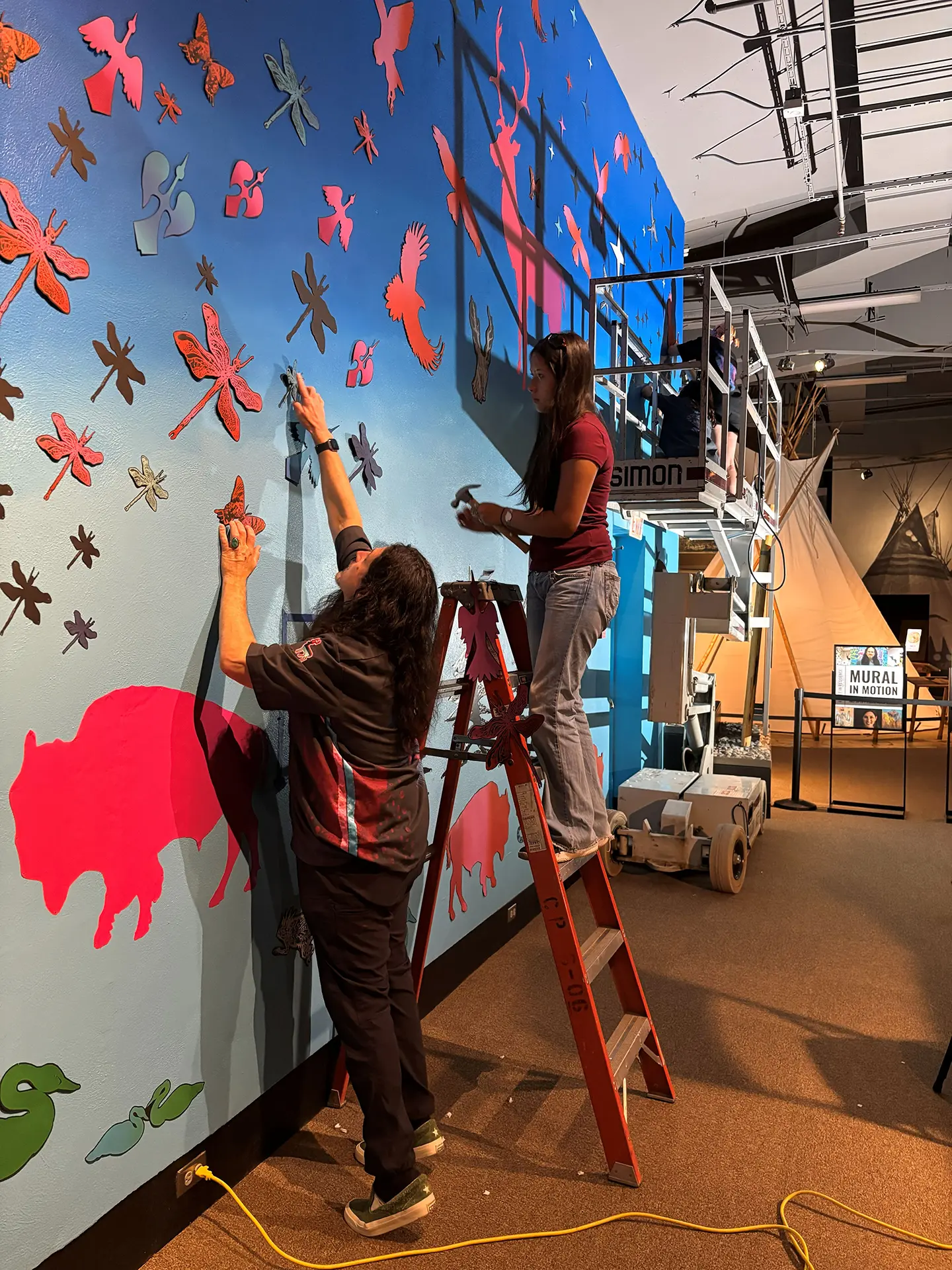 John Hitchcock (left) adds a dragonfly to Buffalo, Deer, Bird, 2025.